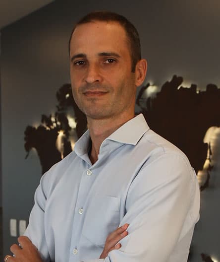 Dr. Fernando Weiss, vestindo camisa social azul clara, com expressão confiante e braços cruzados, em frente a um fundo com mapa estilizado.