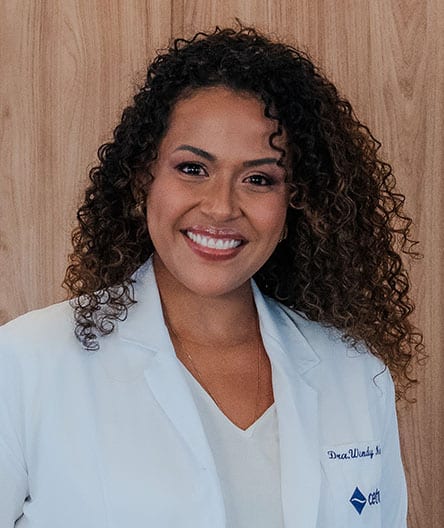 Dra. Wendy Sieerralta, vestindo jaleco branco, sorrindo em frente a um fundo de madeira clara