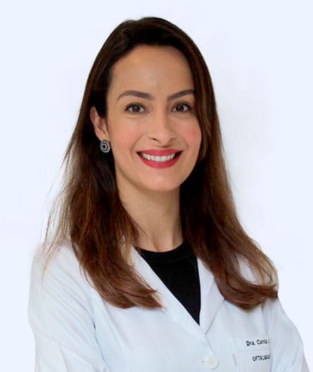 Médica sorridente, vestindo jaleco branco sobre blusa preta, com cabelos soltos e expressão acolhedora.