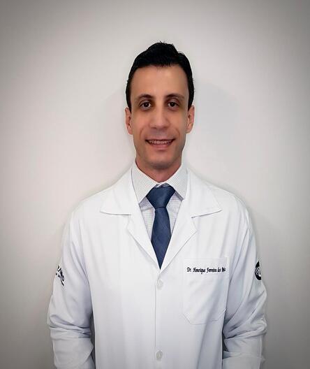 Dr. Henrique Ferreira, vestindo jaleco branco e gravata, docente do curso de Pós-Graduação Lato Sensu em Tomografia e Ressonância em Abdômen e Tórax.