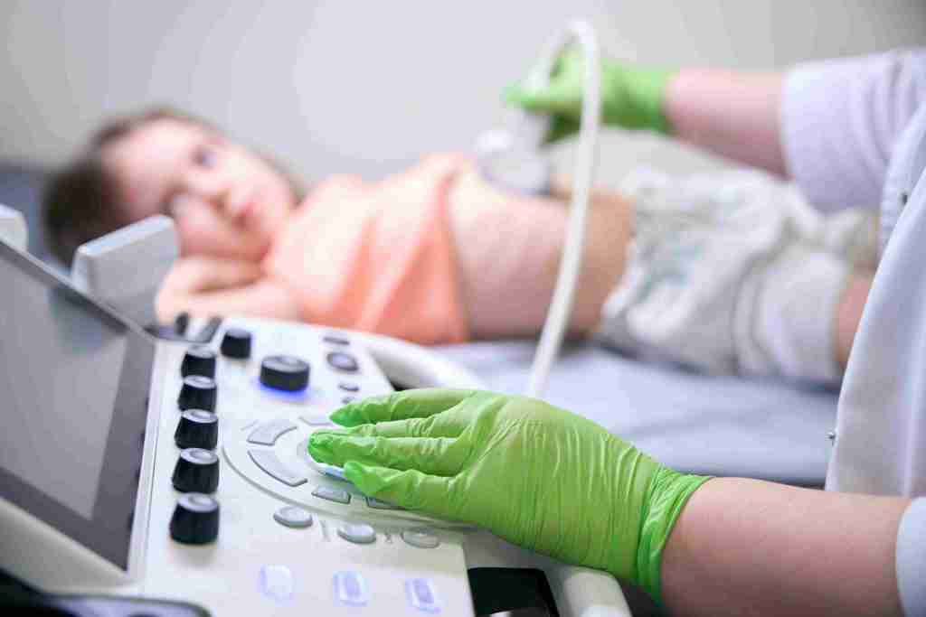 Profissional realiza ecocardiografia pediátrica em criança deitada utilizando aparelho de ultrassom com foco no painel de controle.